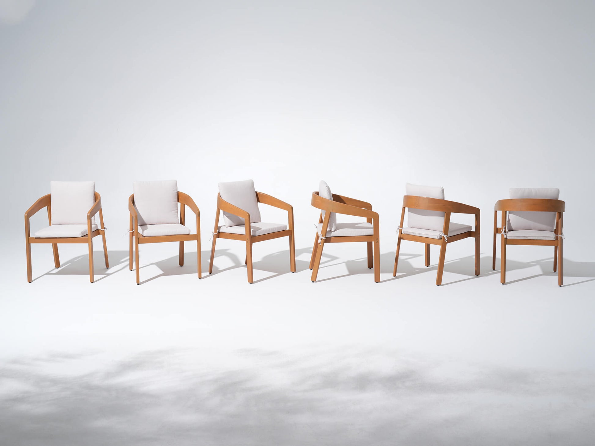 Six wucalyptus wooden dining chairs with white cushions arranged in a row - Sunsitt’s Modern Premium Outdoor Furniture