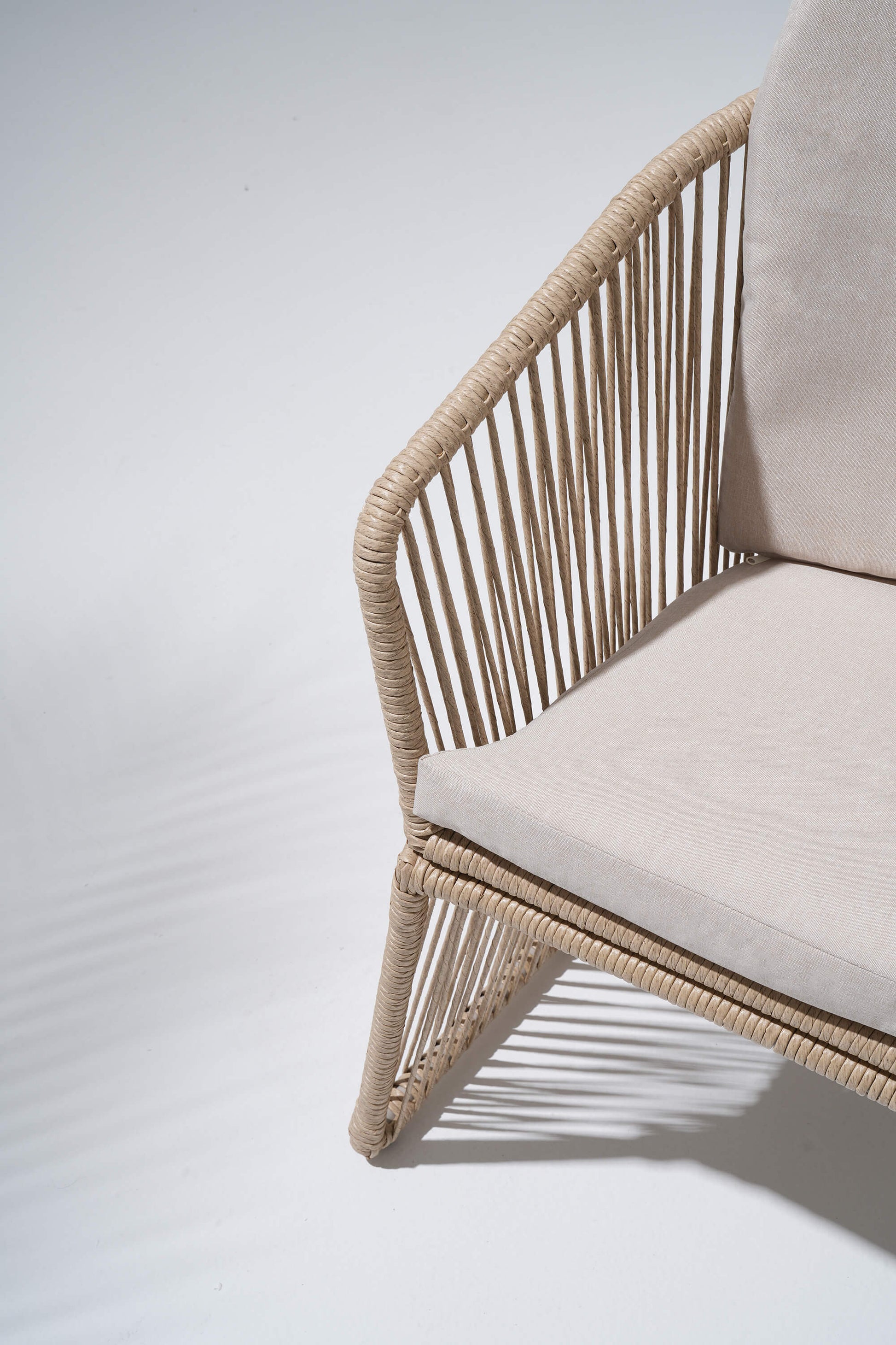 Chair with wicker frame and beige cushion on a light gray background