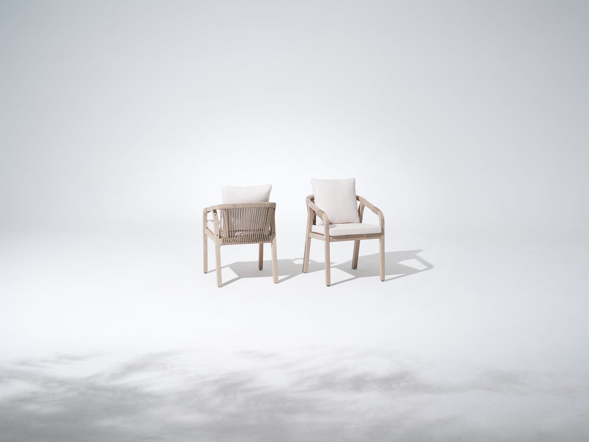 Two wood outdoor dining chairs with white cushions, rope design